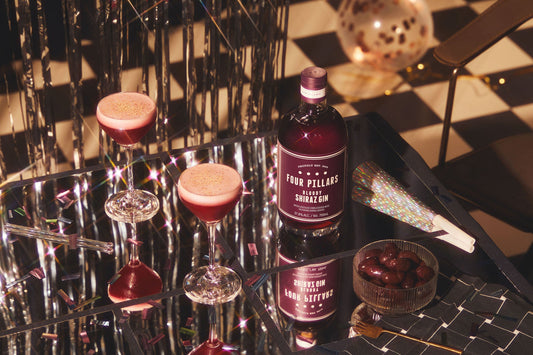 Four Pillars Gin Bloody Shiraz Gin on a reflective table with two Clover Club gin cocktails.