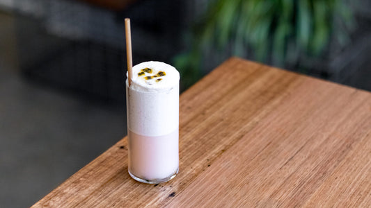 A pink and frothy gin cocktail in a tall glass garnished with passionfruit.