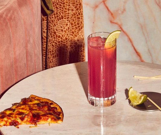 A Four Pillars Gin Bloody Shiraz Ghoul gin cocktail next to a slice of pizza.