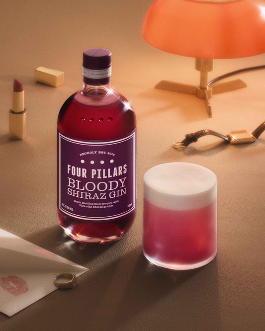 A bottle of Four Pillars Bloody Shiraz Gin and a Bloody Gin Sour cocktail in a short rocks glass.