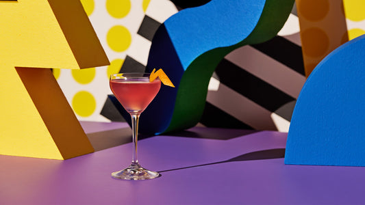 A picture of a bright, pink yuzu gin cosmopolitan cocktail surrounded by bright colours and shapes.