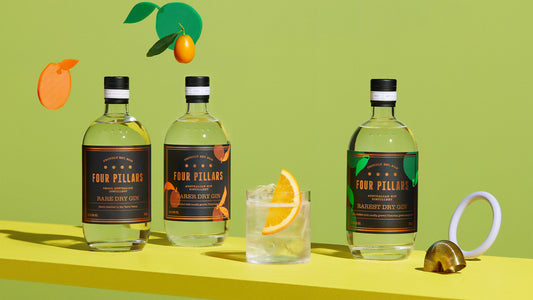 Three bottles of Four Pillars Gin Rare Dry Gin variations, with a gin and tonic with a garnish of lemon in front of a green wall.
