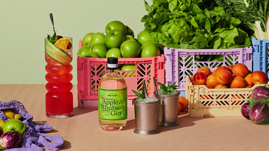 Indulge in A bottle of Four Pillars Gin Green Apple & Rhubarb Gin in front of fresh apples and gin cocktails.