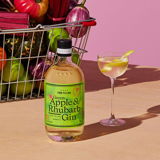 A green apple martini next to a bottle of Green Apple and Rhubarb Gin.