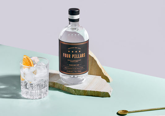 A bottle of Four PIllars Gin Rare Dry Gin next to a simple gin & tonic cocktail with an orange garnish.