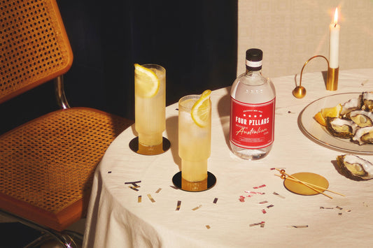 Two warming gin cocktails in two tall glasses on a white table cloth next to a bottle of Modern Australian Gin