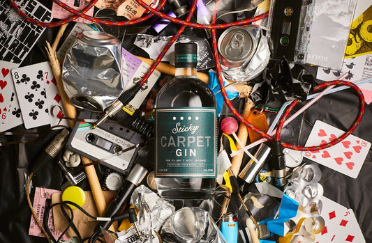 The 2019 Sticky Carpet gin laying on top of a pile of playing cards, mix tapes, and squashed beer cans.