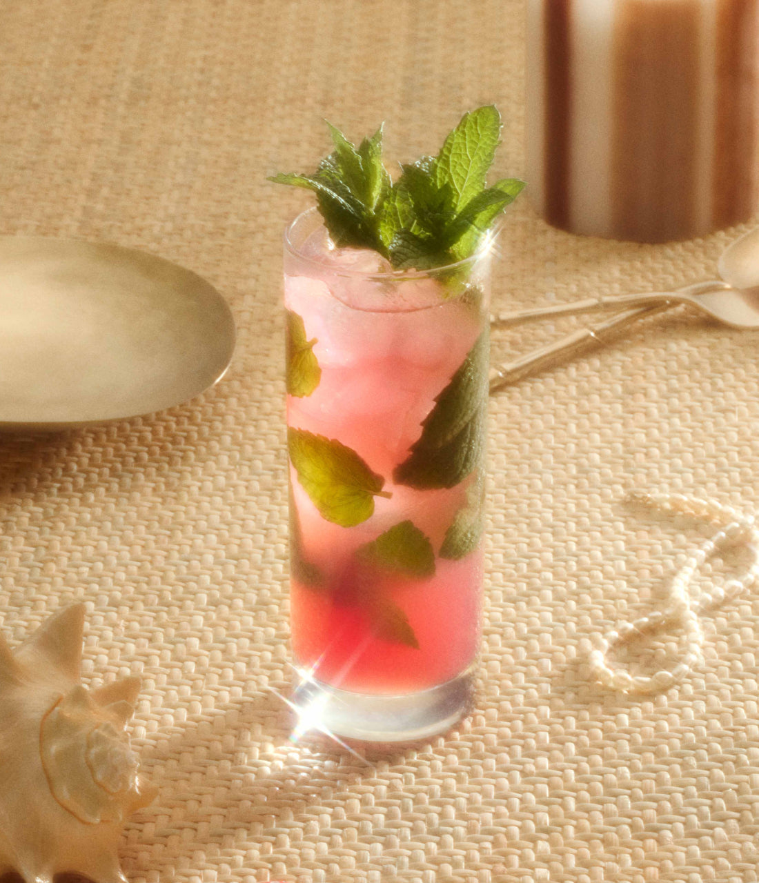 A highball glass containing a Bloody Shiraz Gin Mojito cocktail sits on top of a straw mat.