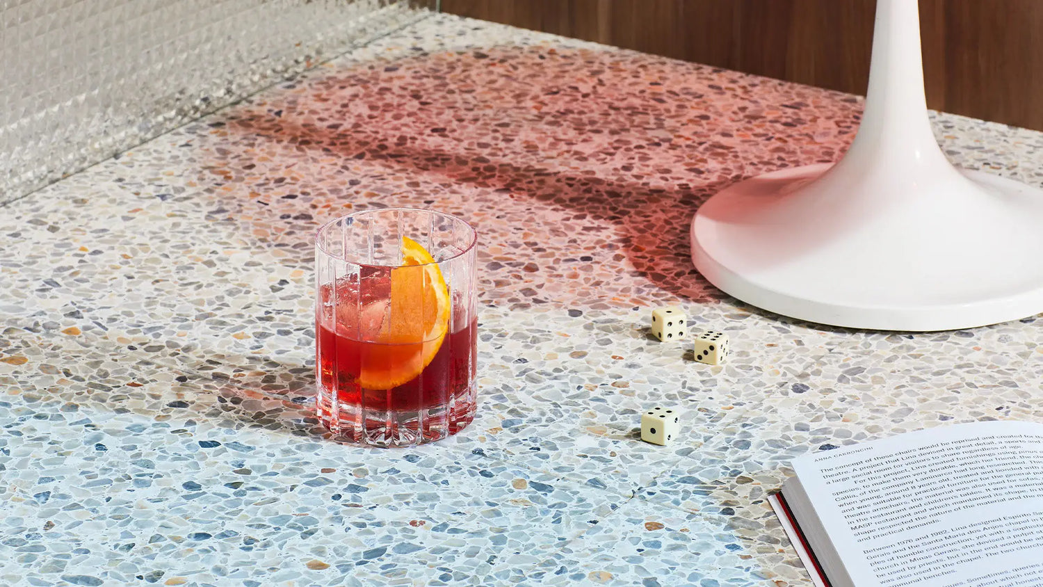 A bright red negroni cocktail with a wedge of orange for garnish presented in a short, crystal glass.
