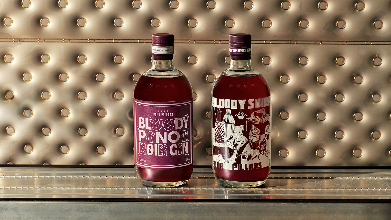 A bottle of Four Pillars' Bloody Shiraz Gin and Bloody Pinot Noir Gin on a bar counter with a decorative wall in the background.
