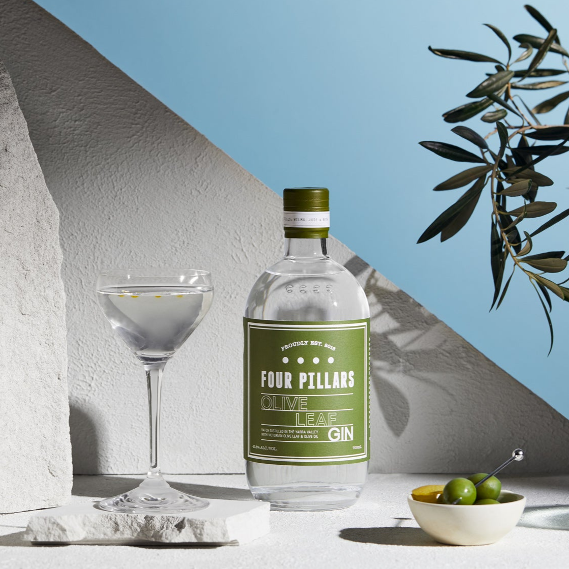 A bottle of Four Pillars Olive Leaf Gin and a Martini garnished with olive oil.