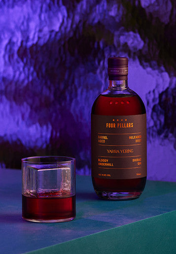 A bottle of Four Pillars Gin Barrel Aged Underhill Shiraz Gin next to a gin cocktail on the rocks