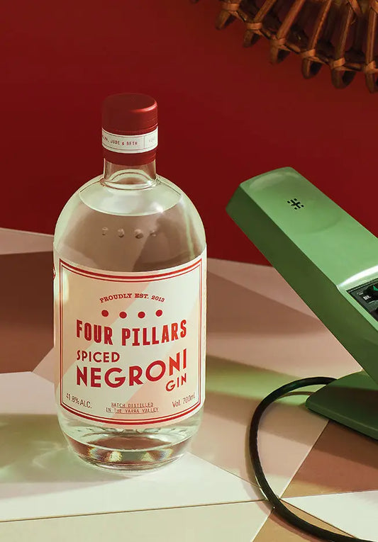 A bottle of Four Pillars Gin Spiced Negroni Gin sitting in a retro, red setting.