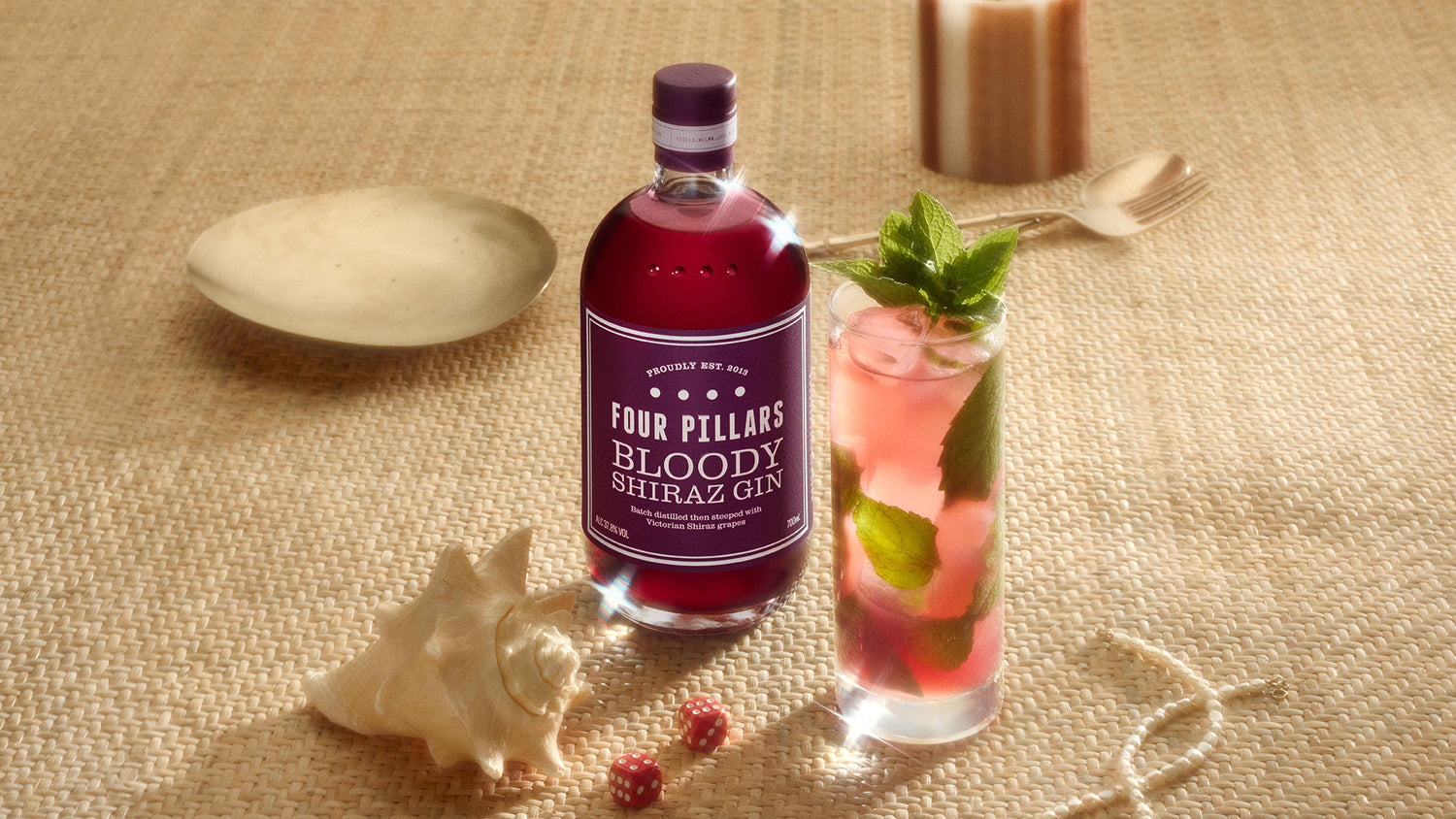 A bottle of Four Pillars Gin Bloody Shiraz Gin next to a delicious Bloody Mojito gin cocktail in a highball glass garnished with mint.