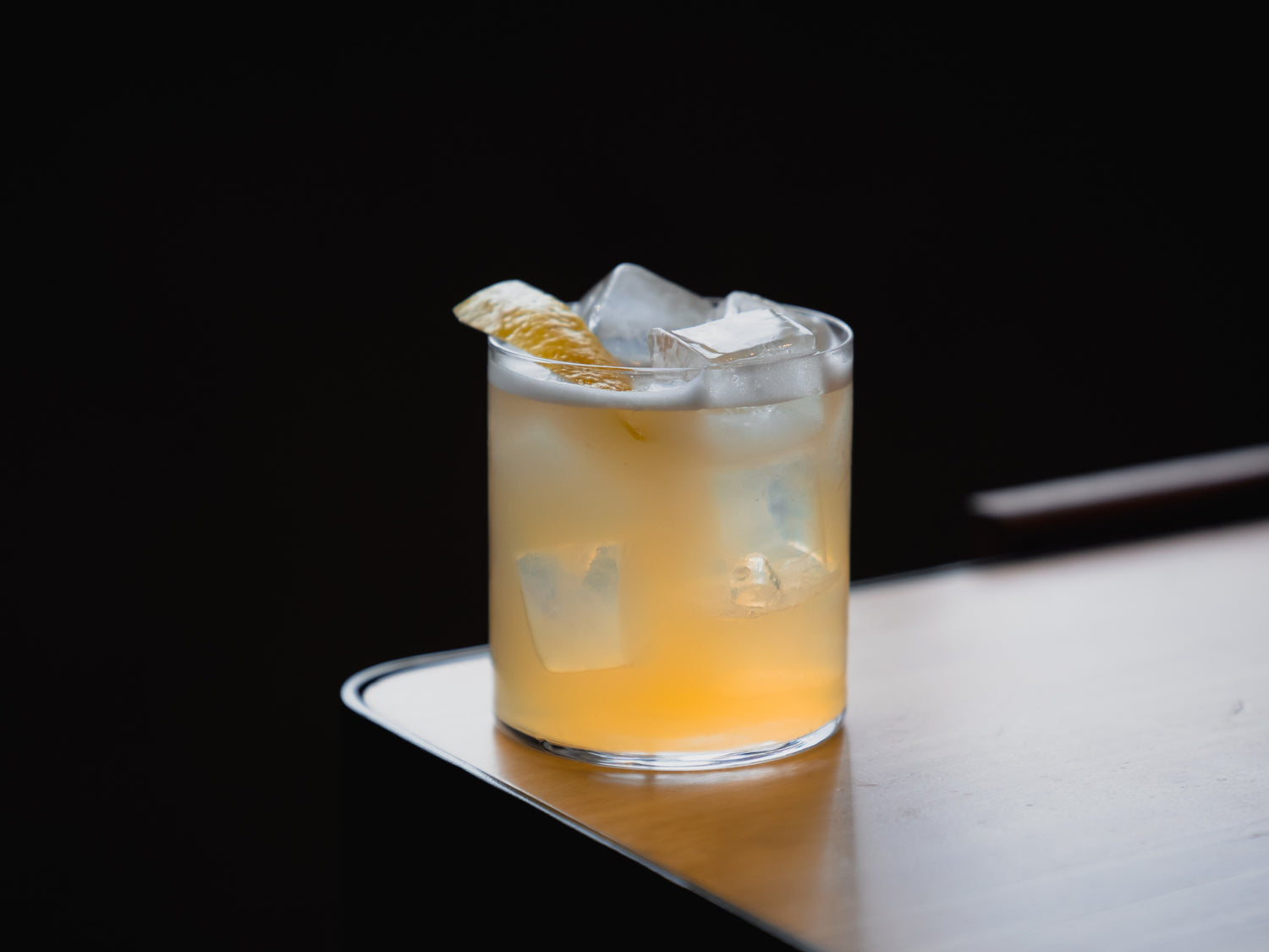 Four Pillars non-alcoholic cocktail with ice in a glass on a dark surface.