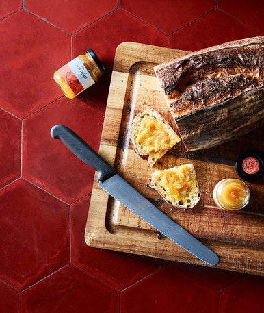A wooden cutting board displaying fresh bread and butter, alongside a jar of Four Pillars gin breakfast negroni flavoured marmalade.