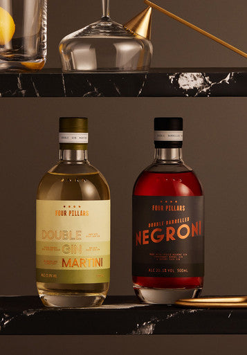 Four Pillars Gins two bottled cocktails, one a ready to drink martini, the other a negroni, sitting on a black marble shelf with fancy glassware.