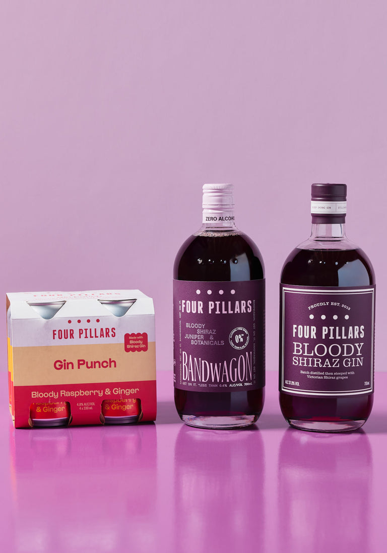 Four Pillars Bloody range featuring a 4-pack of Gin Punch cans, a bottle of Bandwagon Bloody (alcohol-free), and a bottle of Bloody Shiraz Gin, set against a pink background