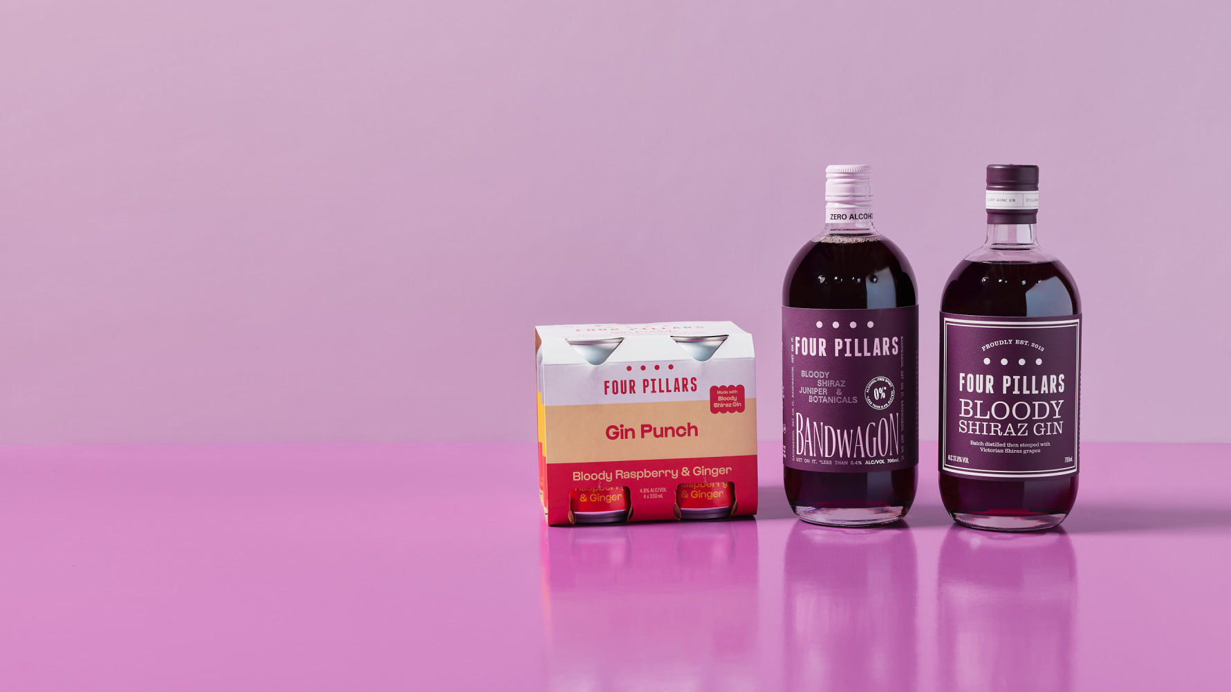 Four Pillars Bloody range featuring a 4-pack of Gin Punch cans, a bottle of Bandwagon Bloody (alcohol-free), and a bottle of Bloody Shiraz Gin, set against a pink background