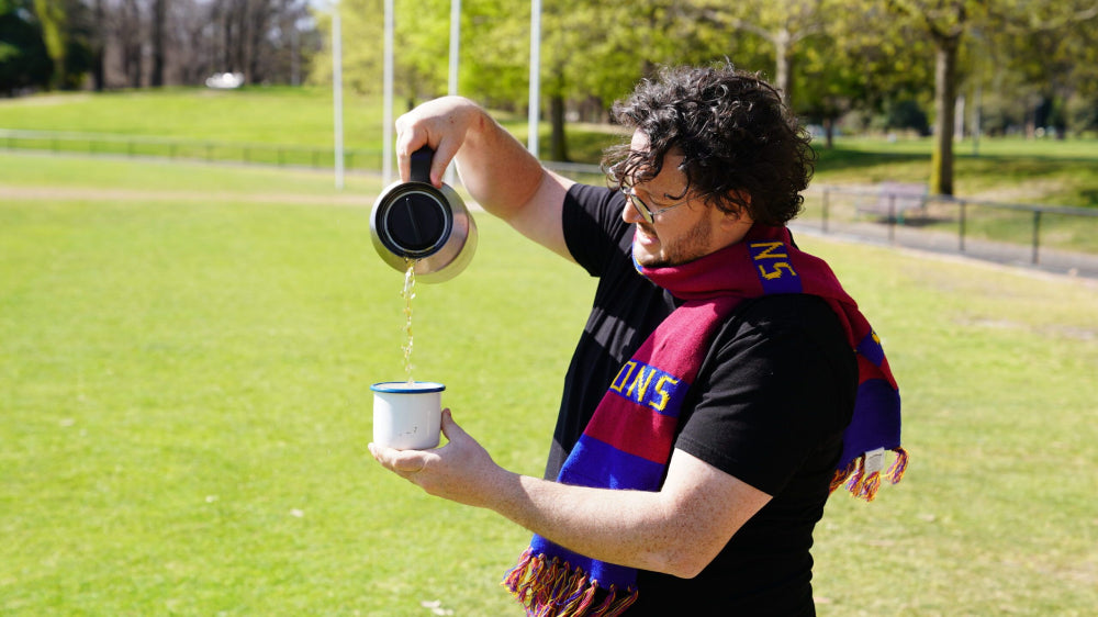 Four Pillars Gin Drinks director Nick Tesar pouring himself a thermos punch gin cocktail wearing a melbourne AFL team scarf.