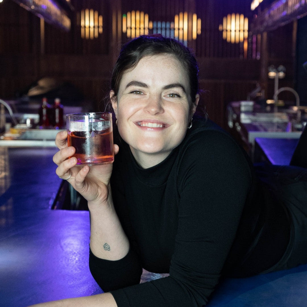 A girl holding a glass of amber liquid in a bar setting with purple lighting at Four Pillars Sydney Laboratory.