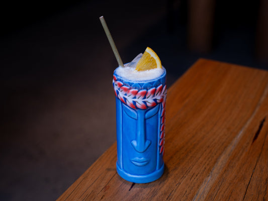 Blue tiki mug containing a non-alcoholic Four Pillars drink on a wooden surface.