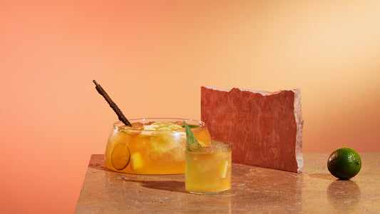 Christmas Gin punch in a large punch bowl with a rocks glass filled with the cocktail and garnished with a pineapple leaf.