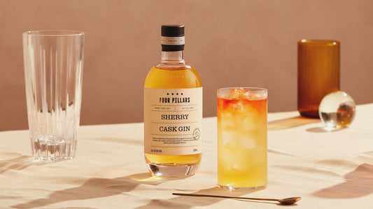 A bottle of Sherry Cask Gin and a dark n' stormy cocktail in a tall glass beside it. 