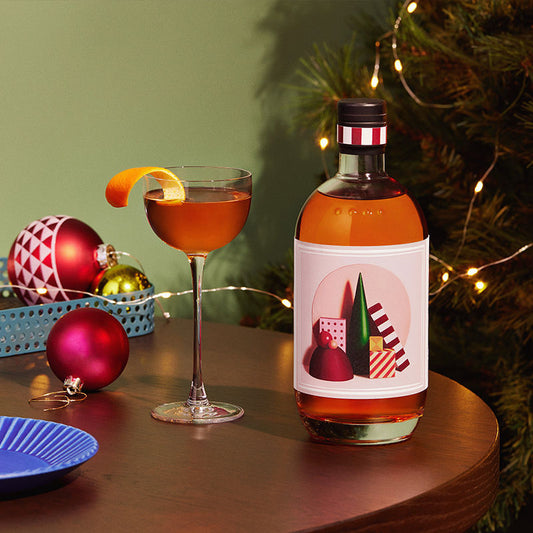 Four Pillars Gin Australian Christmas Gin next to a gin cocktail with an orange garnish, in front on a Christmas tree.