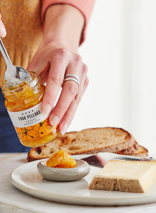 A hand spreading Four Pillars gin marmalade which was made from gin, next to a block of moonshine cheese.