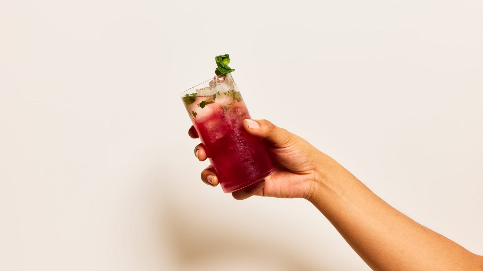 An outstretched hand holding a tall glass containing a Bloody Mojito cocktail made with Four Pillars Bloody Shiraz Gin