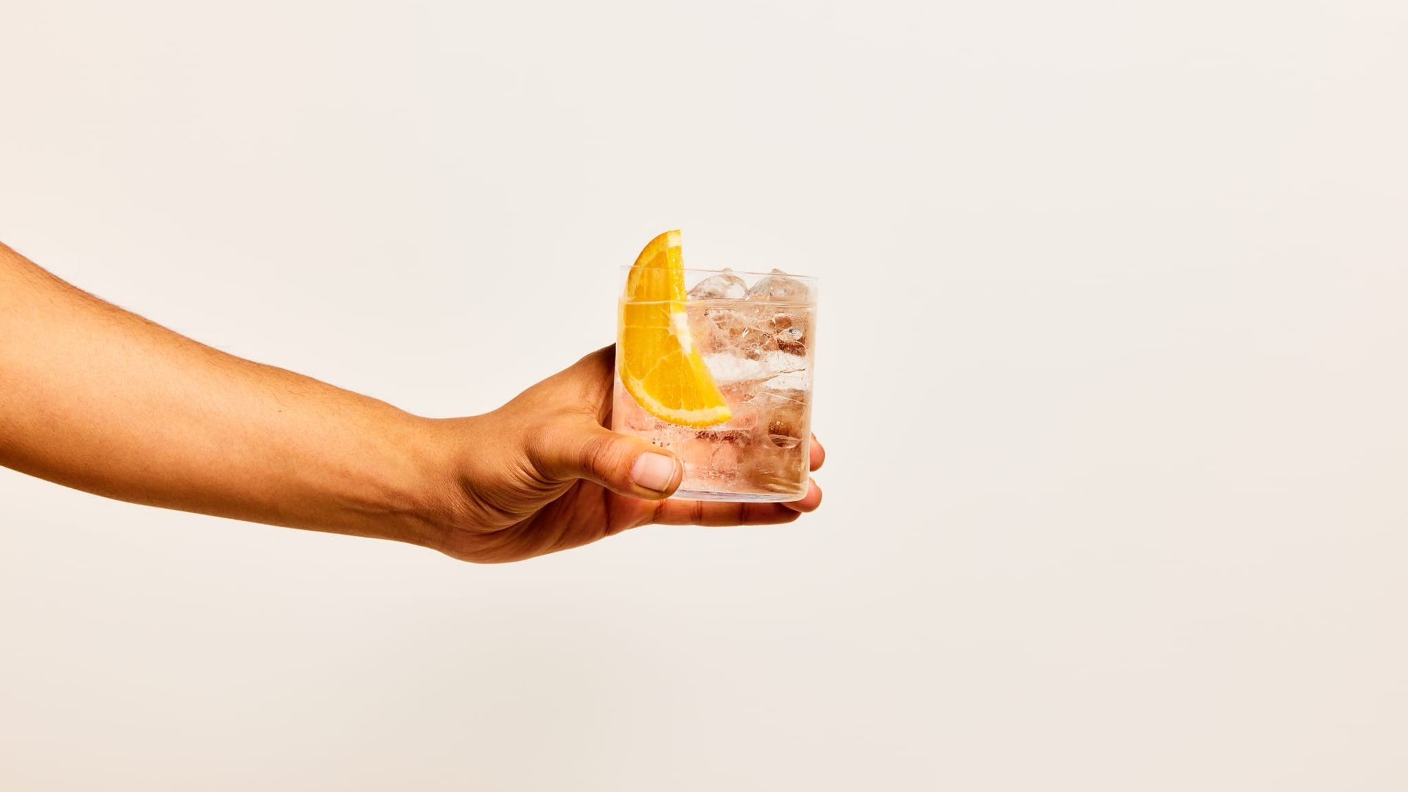 An outstretched hand holding a Four Pillars G&T made with Rare Dry Gin and garnished with an orange.