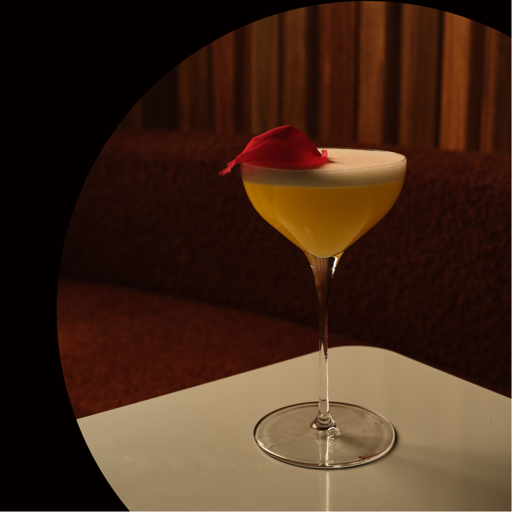 Cocktail in a glass with a red garnish on a table, with text about a Japanese-inspired bar in the background.
