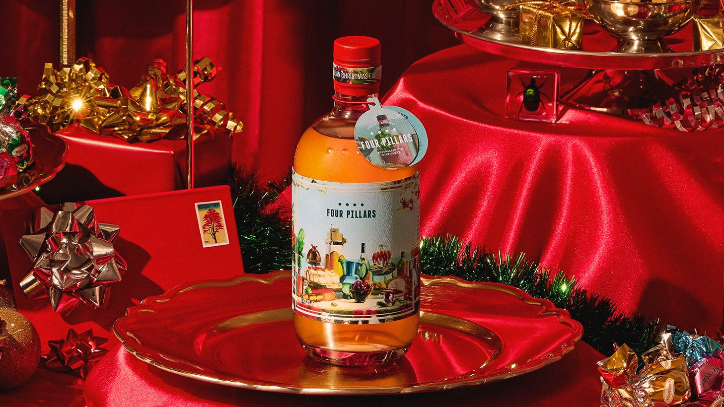 Bottle of Four Pillars Australian Christmas Gin on a silver dish sitting on a table covered in red Christmas decorations.