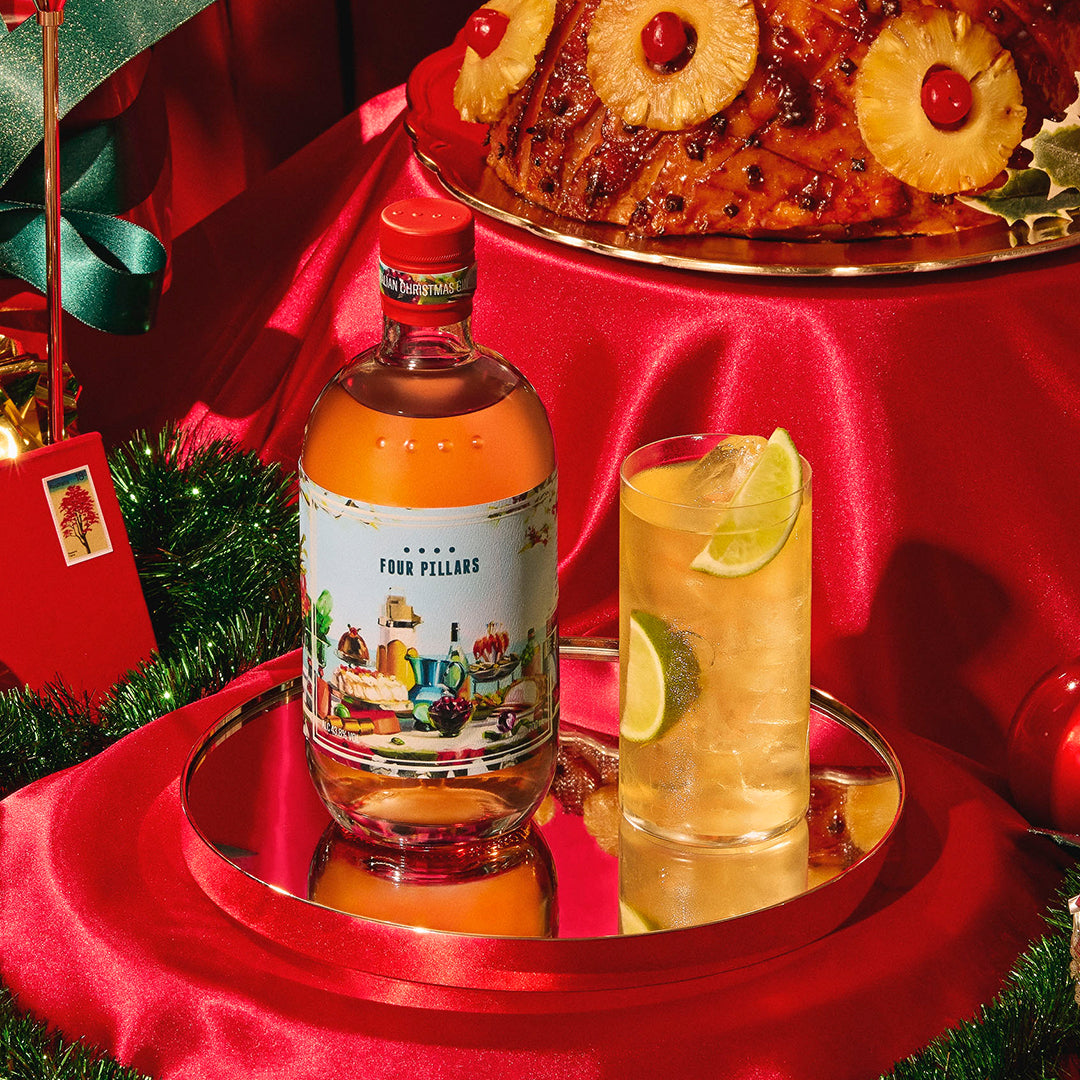 Bottle of Four Pillars Christmas gin with a cocktail and Christmas decorations on a red tablecloth.