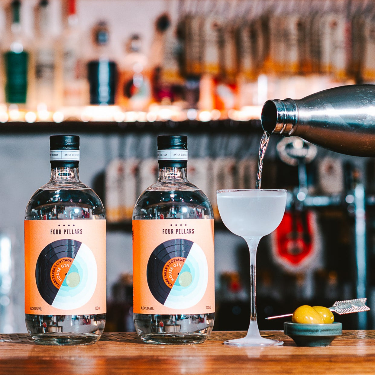 Bottles of Four Pillars x Caretaker's Cottage Gin on a bartop next to a cold Martini being poured from a flask.