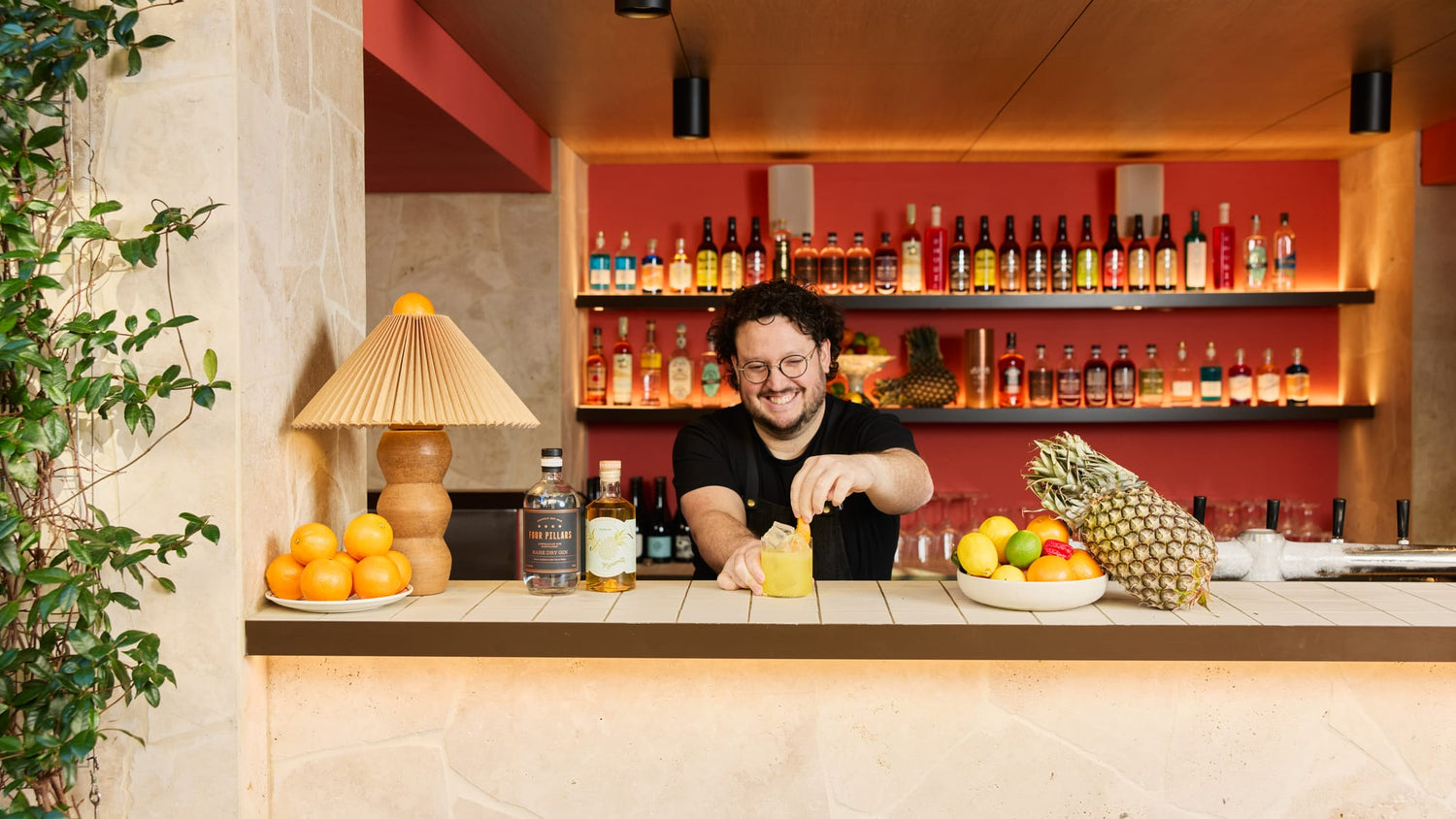 A bartender standing behind a bartop serves up an orange cocktail made with Four Pillars Rare Dry Gin and Marionette Pineapple Liqueur.