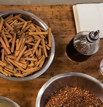 A close up, birds eye view of a wooden bench top with bowls of Australian botanicals and a bottle of gin.