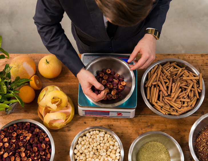 A man weighing out a variety of Australian botanicals including cinnamon sticks, quandong, macadamia, lemon peels and hops.