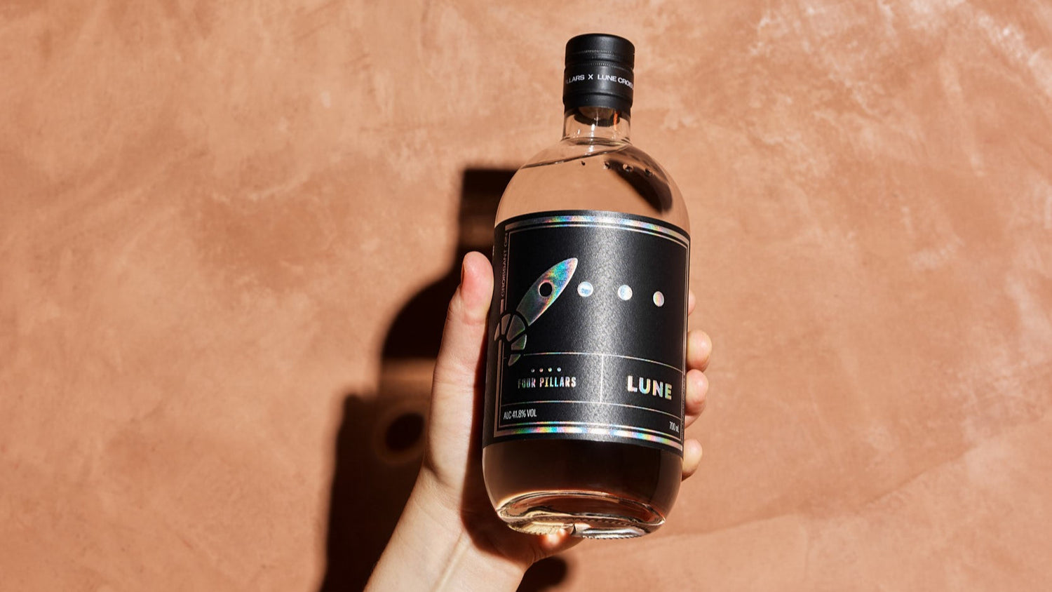 A hand holding a bottle of Four Pillars x Lune Croissant Gin