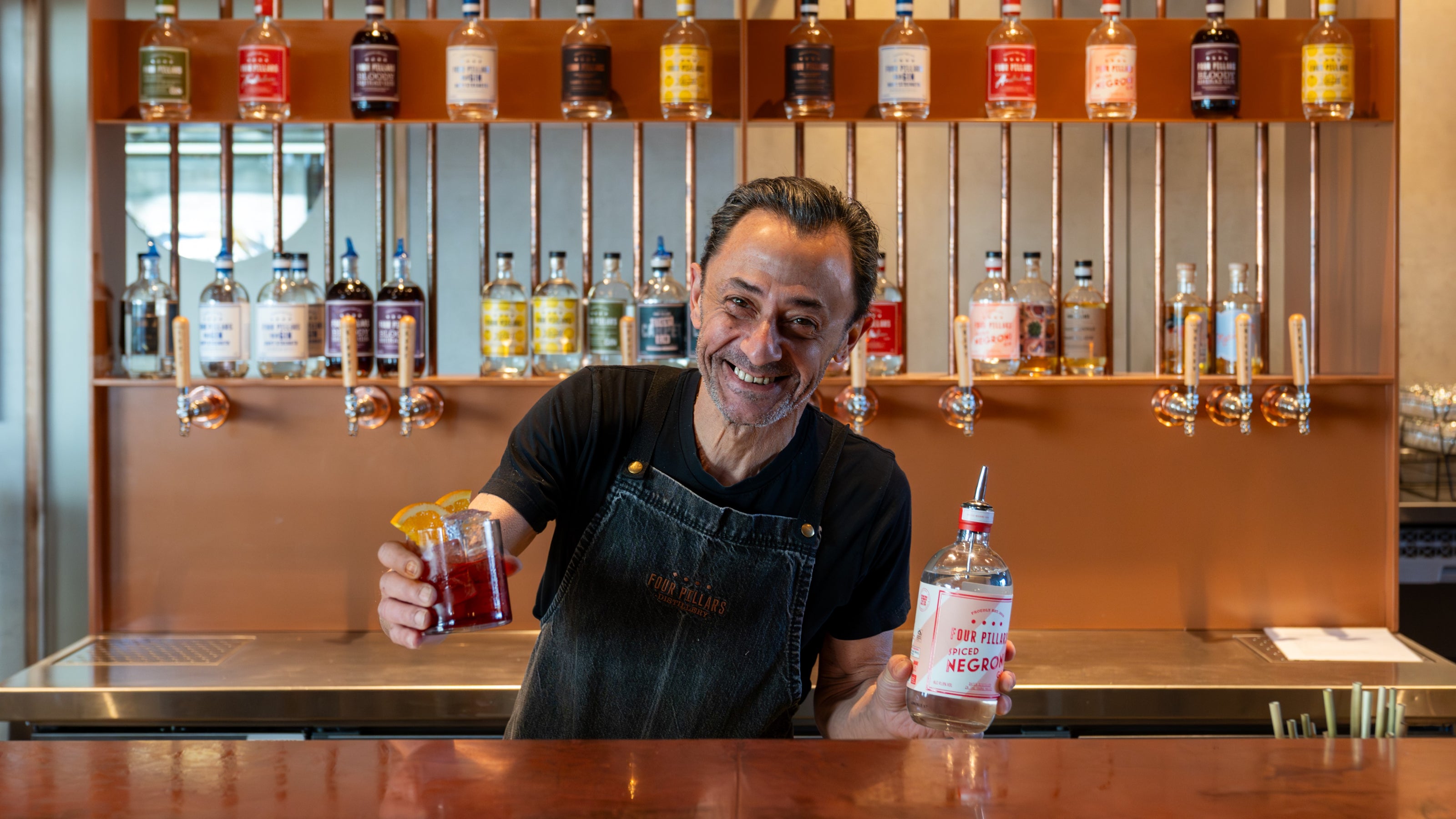 A Four PIllars staff member holds a glass filled with a Negroni and a bottle of Spiced Negroni Gin.