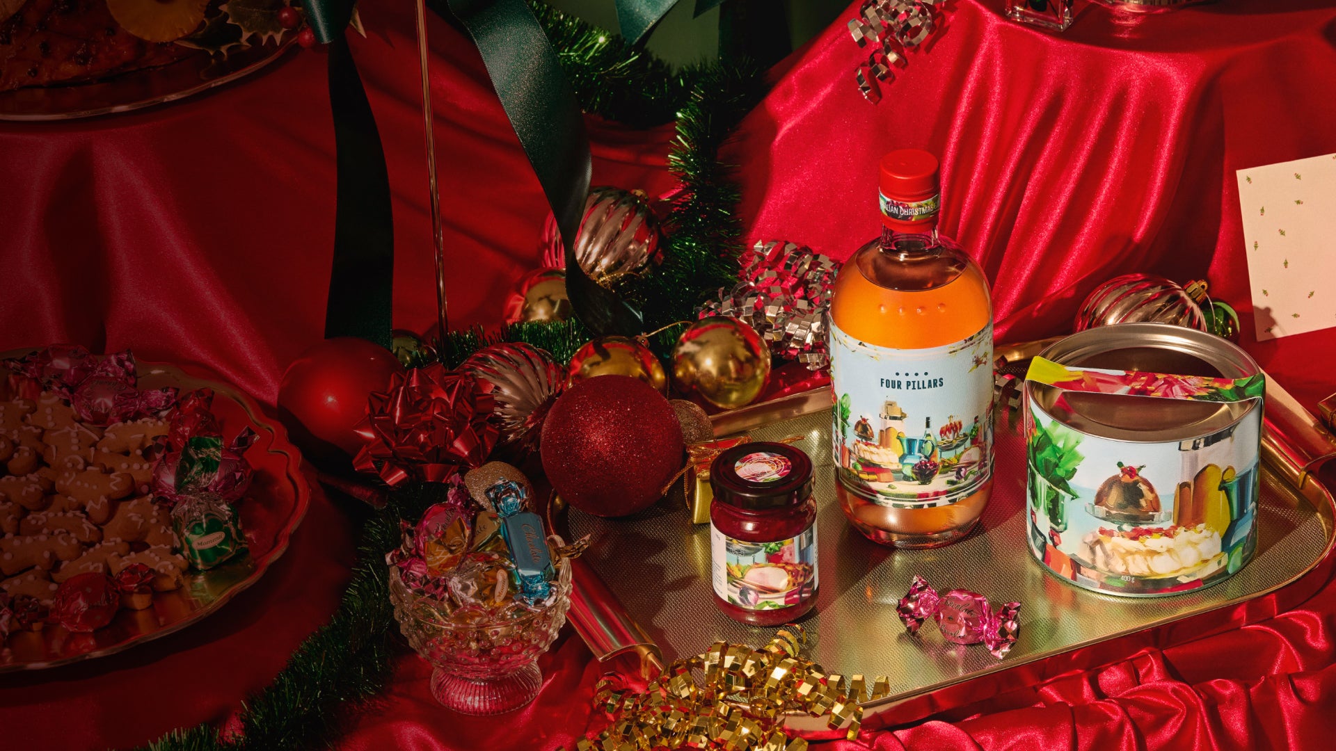 Beverage bottles and jars on a tray with festive decorations and red fabric in the background