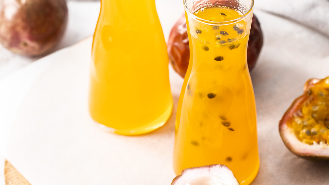 A carafe filled with passionfruit syrup and surrounded by cut and uncut passionfruits.