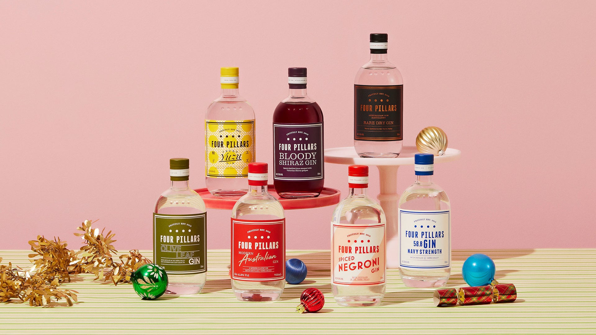 Four Pillars Gin Corporate Gifting range including Fresh Yuzu Gin, Bloody Shiraz Gin, Rare Dry Gin, Olive Leaf Gin, Modern Australian Gin, Spiced Negroni Gin and Navy Strength Gin on a striped green and yellow table cloth surrounded by tinsel and Christmas decorations. 