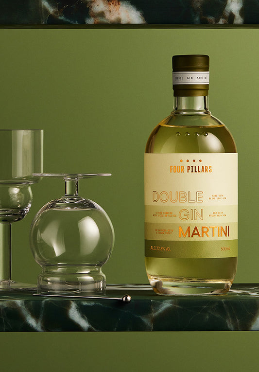 A ready to drink gin cocktail in a stylish bottle of gin next to a glass on a wooden table, ready for a refreshing drink. The label reads Four Pillars Gin Double Gin Martini.