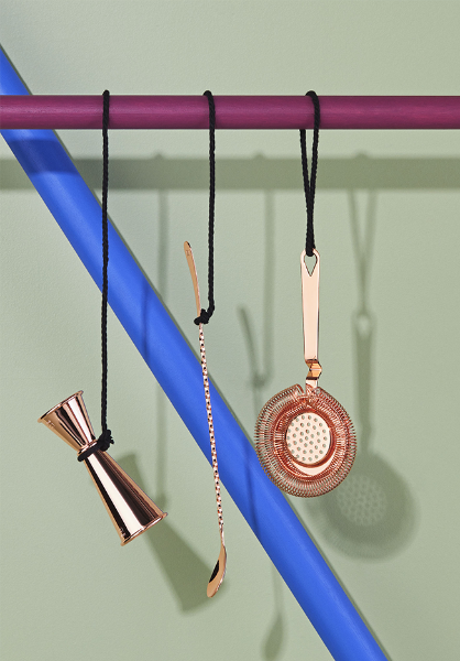 A colorful blue and purple line displays a copper jigger, stirring spoon, and strainer, showcasing essential barware tools.