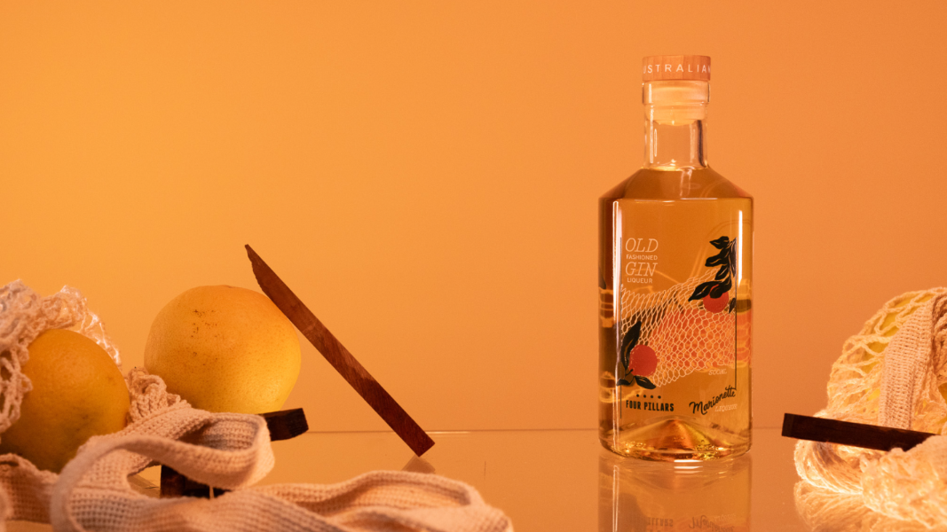 A beautifully designed bottled cocktail, old fashioned gin liqueur, surrounded by string bags of oranges and two bar blades. 